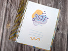 a spiral-bound notebook with a colorful cover, resting on a wooden surface.